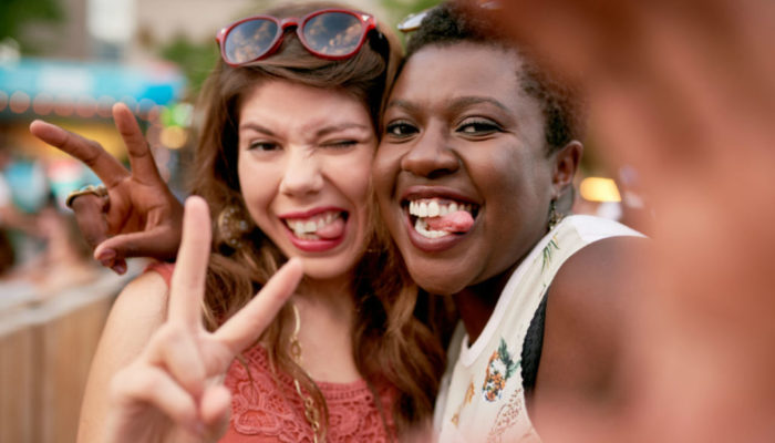 two-women-taking-selfies-in-a-crowd-AdobeStock_174731987